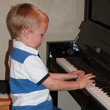 Okan Piano Academy young boy in striped shirt at piano Okan Piano Academy young boy in striped shirt at piano
